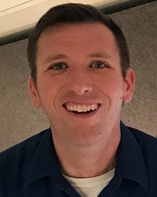 Headshot of Ryan smiling with short dark hair and blue collared shirt.